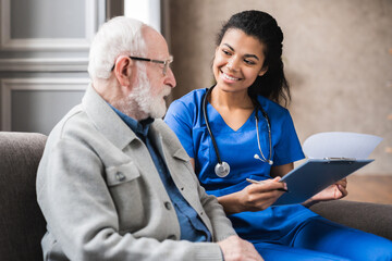 A nurse and an elderly man sitting in front of each other.